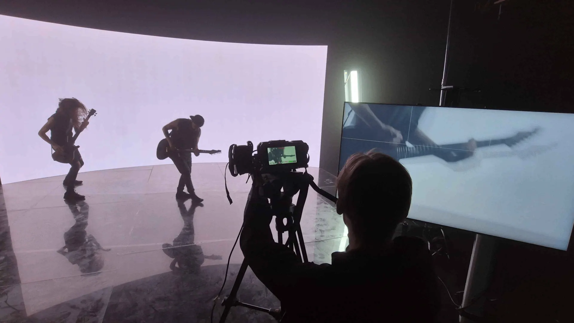 BTS: Two guitarists on the curved LED stage, with a camera and monitor in view.