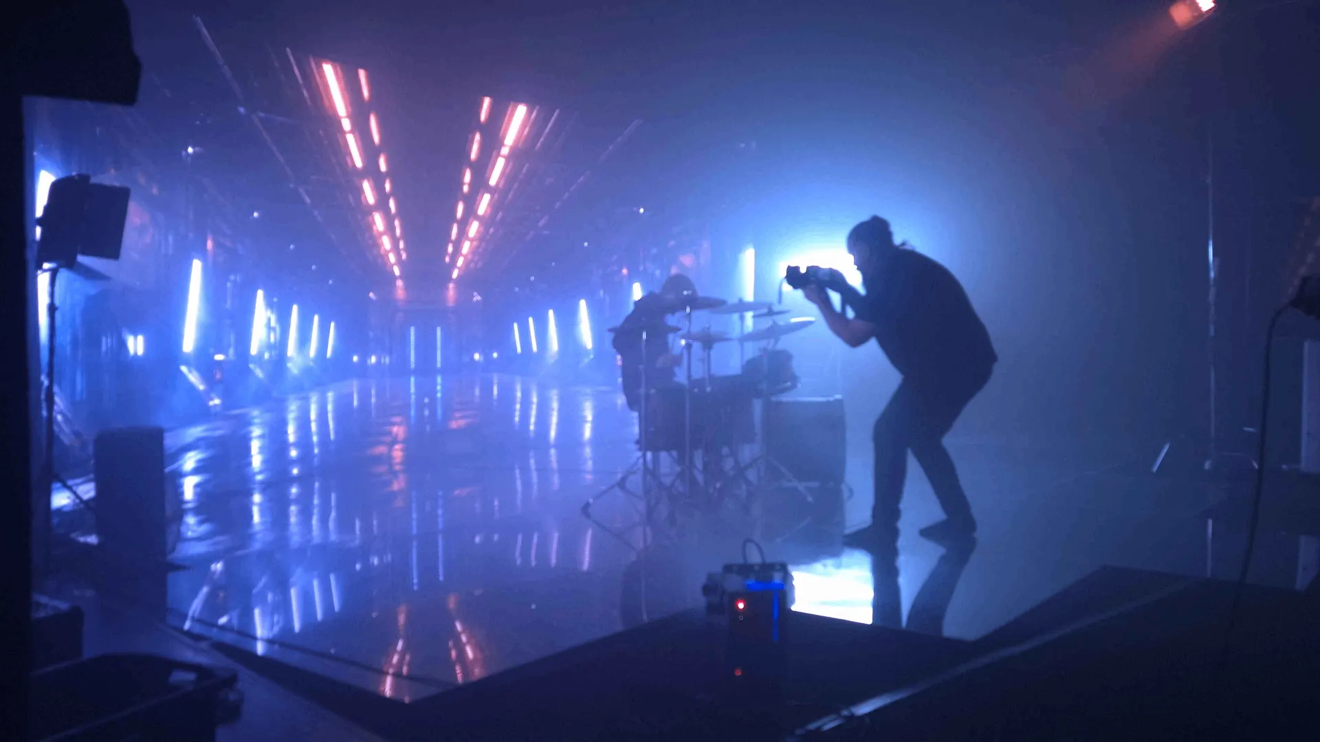 BTS: A neon LED tunnel with a drummer and camera operator in silhouette.